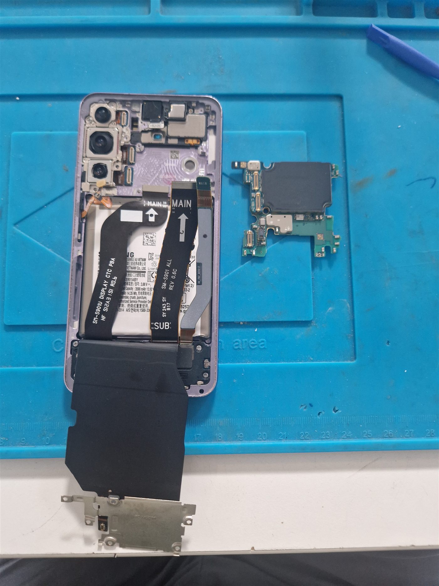 Carte mère du Galaxy S22 extraite et posée au-dessus du châssis sur le tapis d'atelier